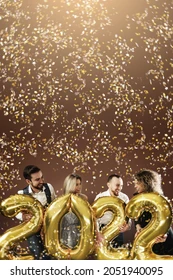 Group of party people celebrating arrival of 2022 New Year with a golden balloons and falling confetti